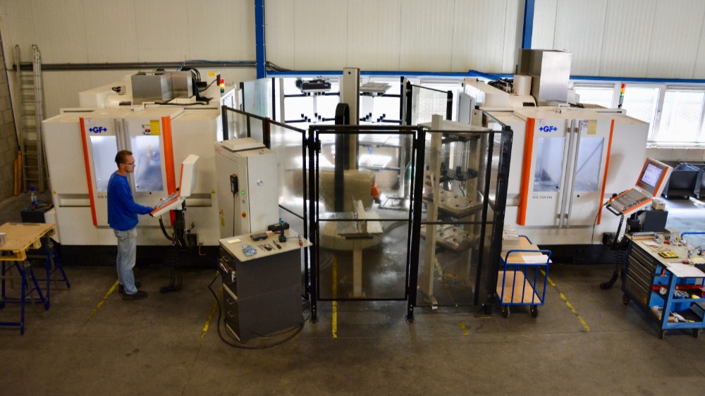 In de werkcel draait de robot tussen de beide freesmachines, met daartussen de drie magazijnzuilen en het beladings- en ontladingsstation