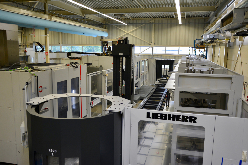 Een robot (centraal) beweegt op rails tussen de twee freesmachines (links) en het palletmagazijn (rechts). De complete werkcel is zo’n 20 meter lang en 10 meter breed